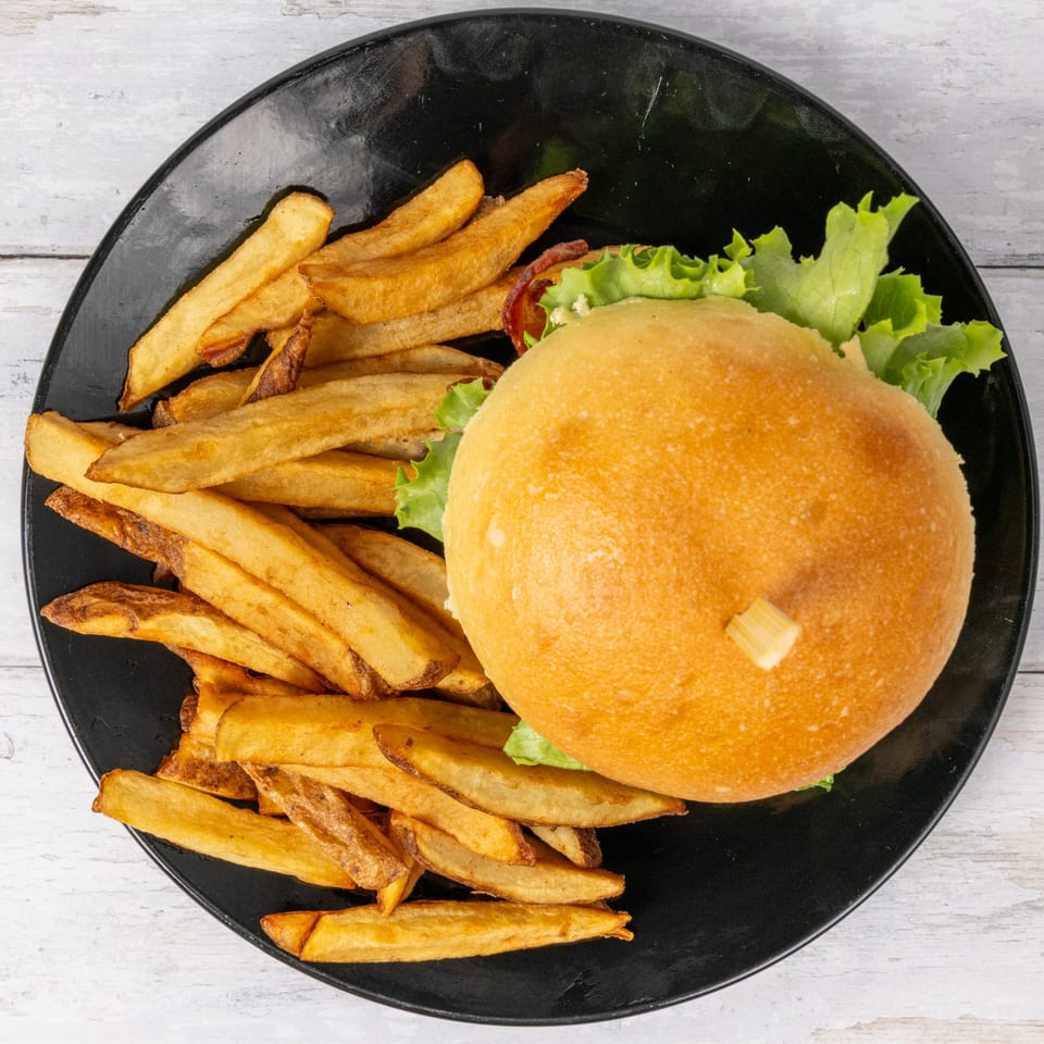 F. Ottomanelli burger with lettuce and a side of golden Belgian fries on a black plate.