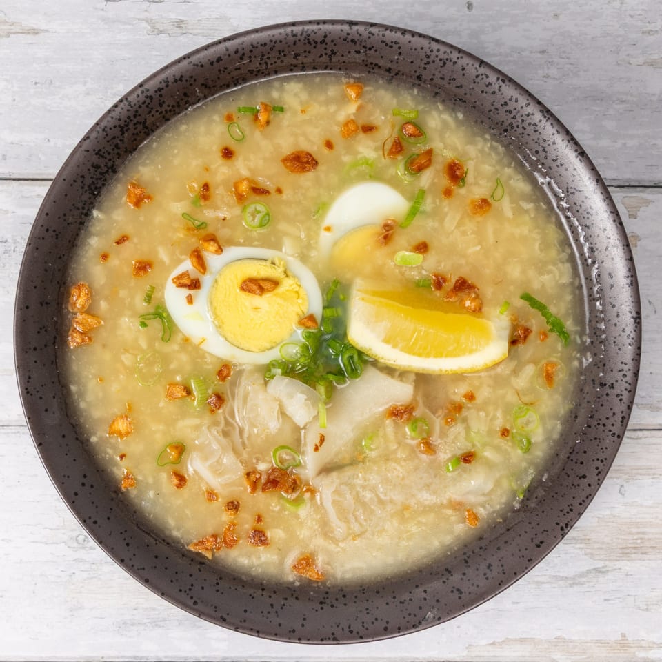 A bowl of creamy soup with sliced hard-boiled eggs, lemon, fried garlic, and green onions.