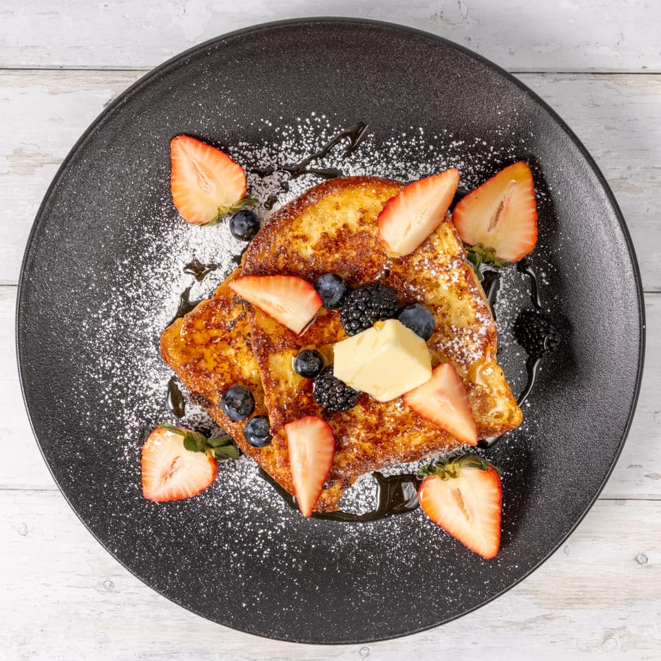 Golden French toast with butter, strawberries, blueberries, and blackberries, dusted with powdered sugar.