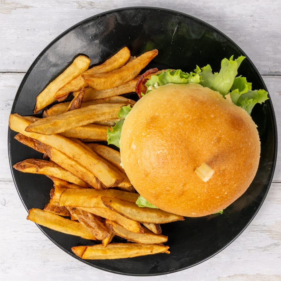 F. Ottomanelli burger with lettuce and a side of golden Belgian fries on a black plate.