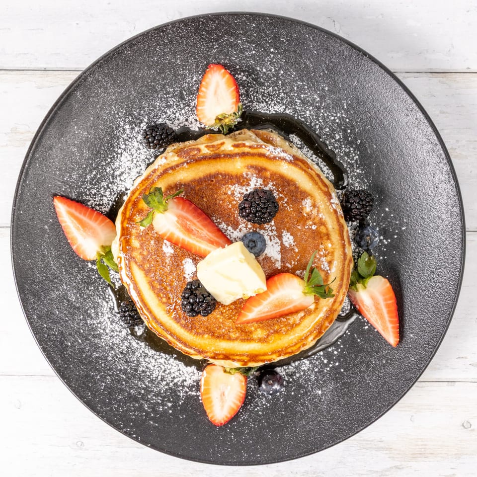 Stack of golden pancakes with butter, strawberries, blueberries, and blackberries on a black plate.